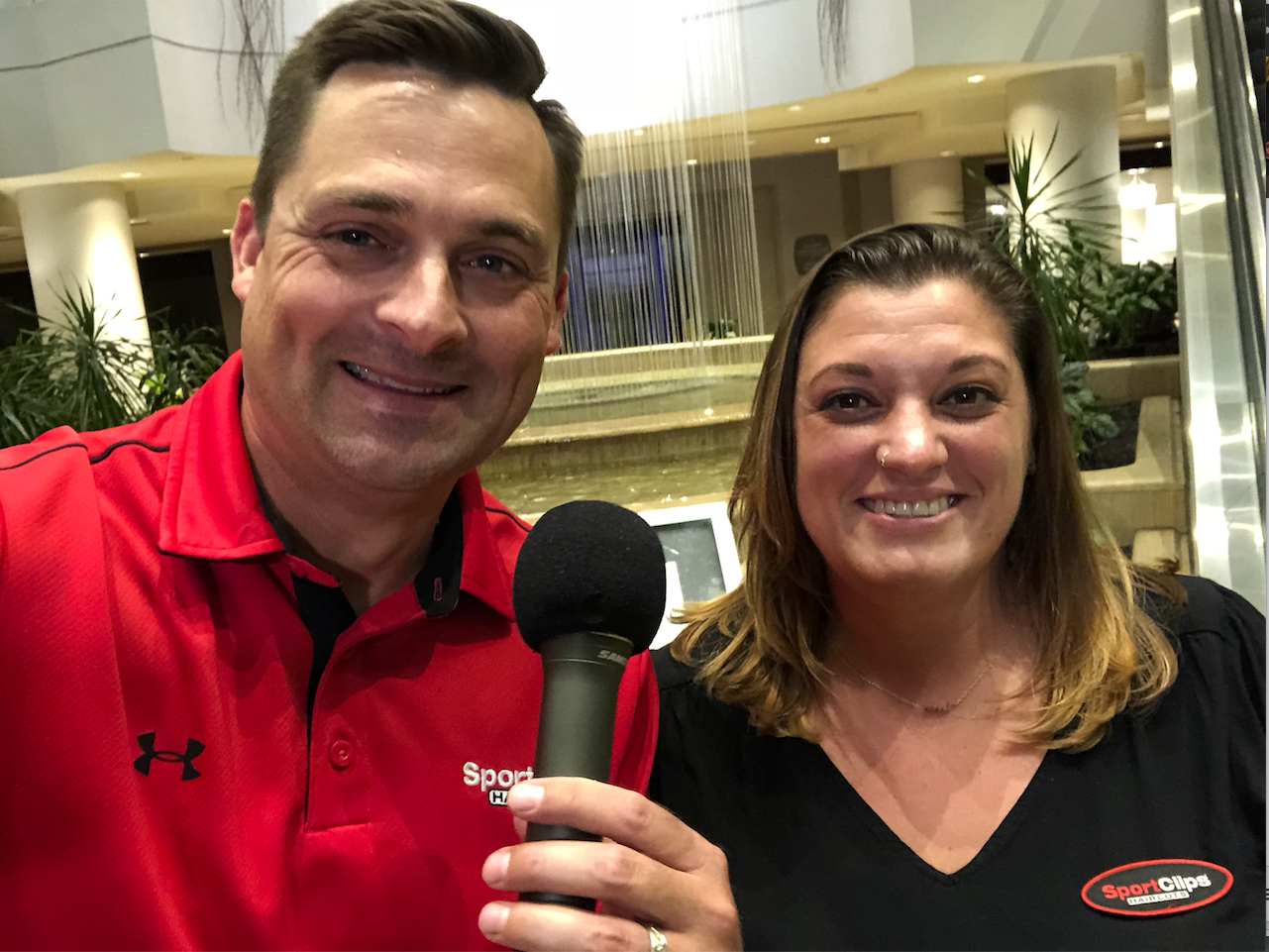 Chad Jordan and Meghan Blanchette holding a microphone in front of a water fountain